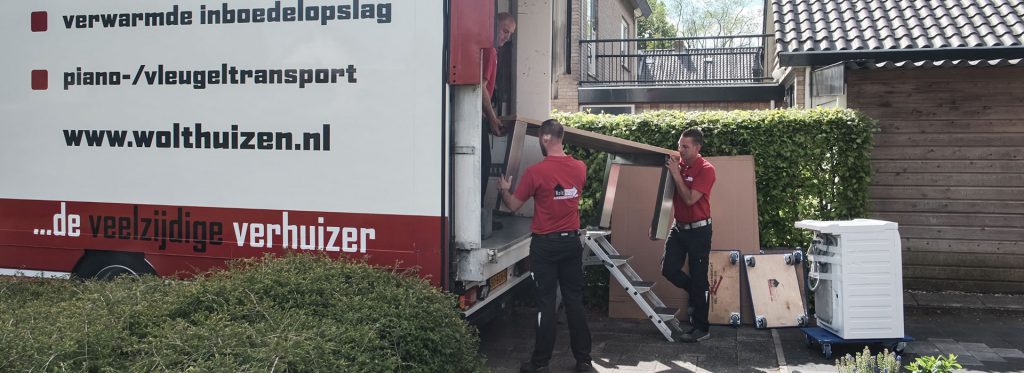 Drie personen laden een tafel en andere meubels uit, uit de vrachtwagen van Wolthuizen